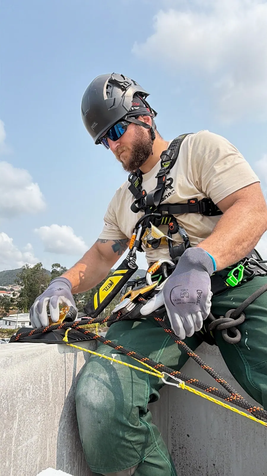 Técnico da RopeX sentado na platibanda a ajustar o descensor na corda antes da descida