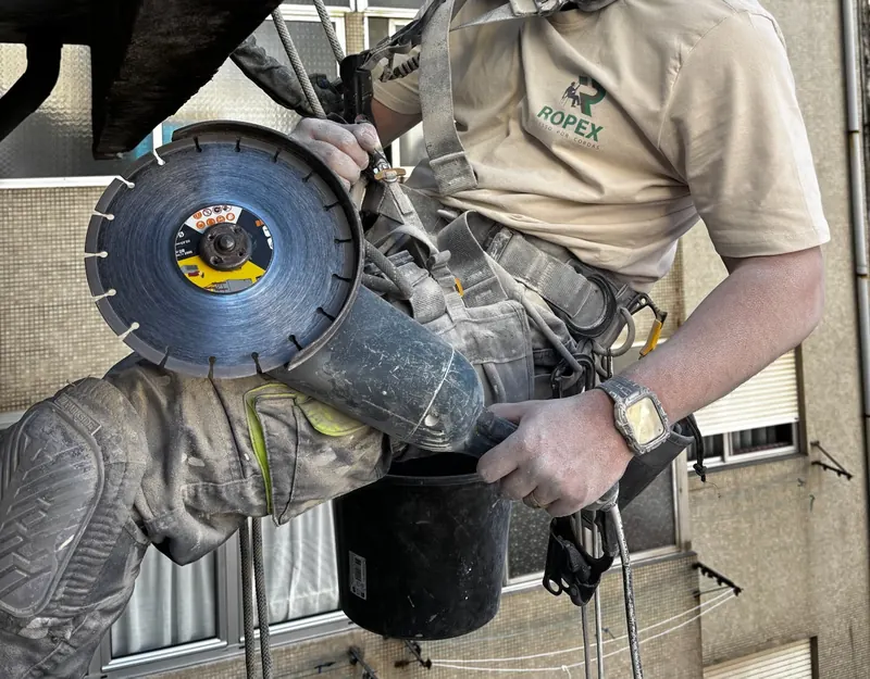 Técnico da RopeX, de polo com o logótipo da empresa, com uma rebarbadora de disco diamantado junto à laje de uma varanda
