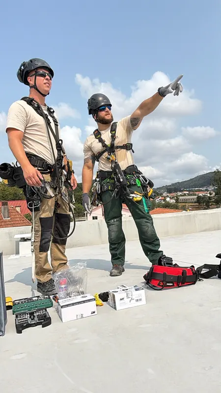 Dois técnicos da RopeX equipados na cobertura de um edifício, um deles a apontar ao longe