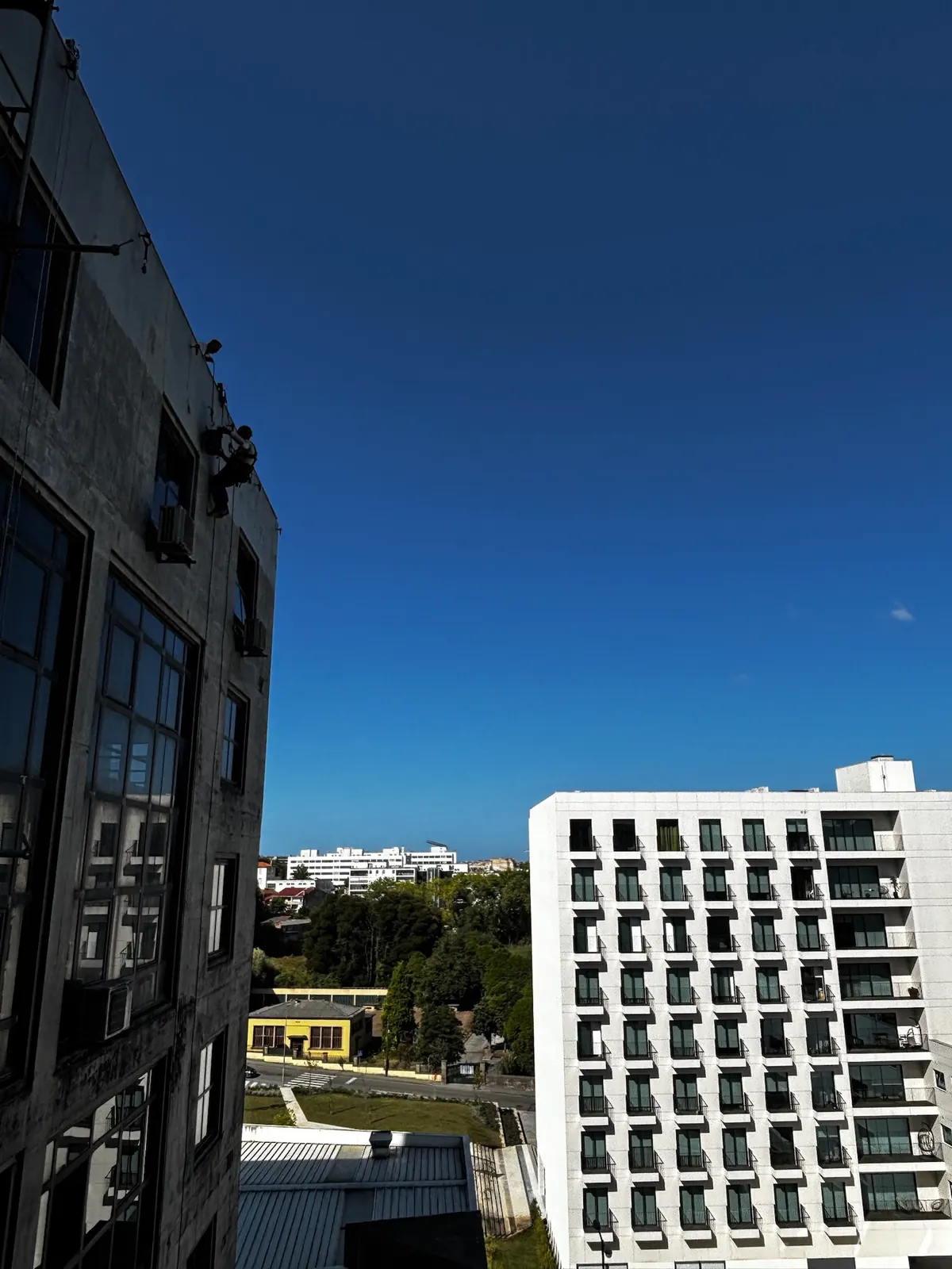 Técnico da RopeX suspenso junto ao topo de um edifício alto, com a cidade lá em baixo