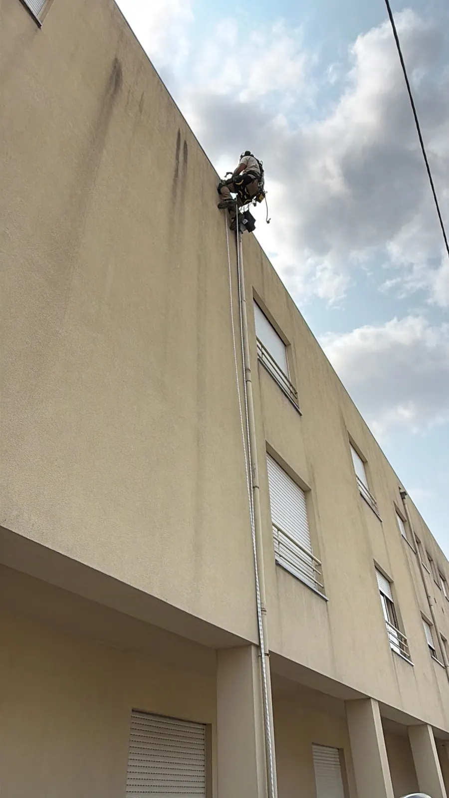 Fachada de um edifício vista da rua, com o técnico da RopeX suspenso lá no alto