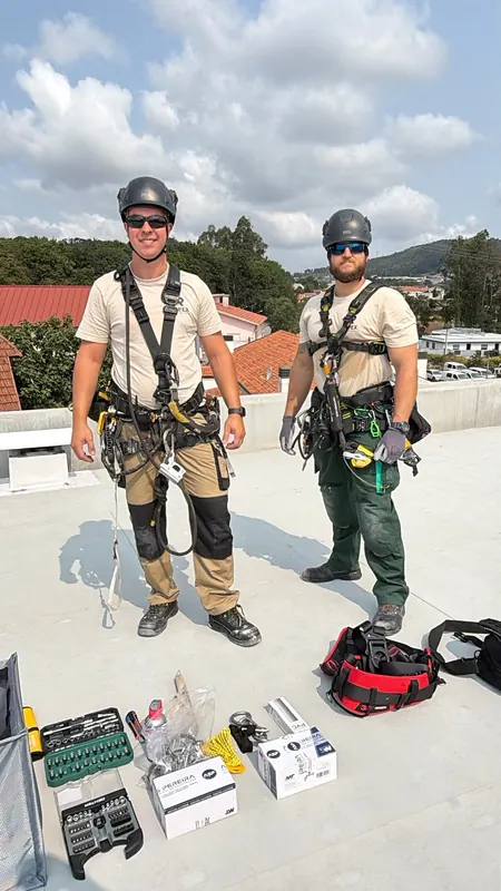 Dois técnicos da RopeX de capacete e arnês na cobertura de um edifício, com o equipamento pousado no chão
