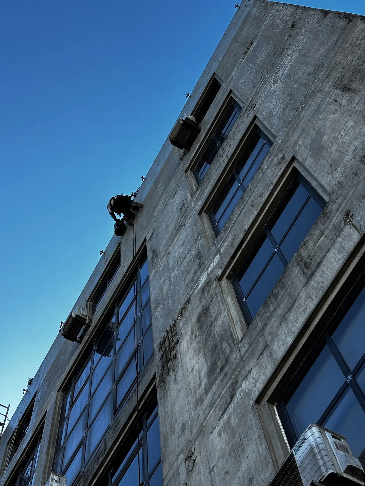 Fachada de betão e vidro de um edifício alto com um técnico da RopeX suspenso por cordas