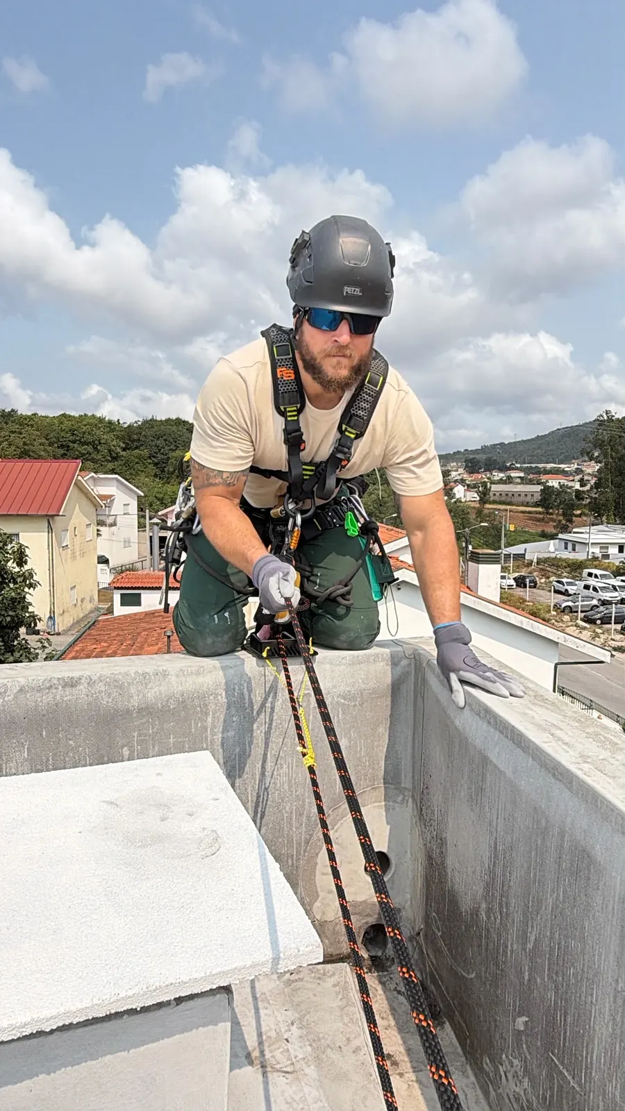 Técnico da RopeX ajoelhado no topo da platibanda, com a mão na corda, no início da descida