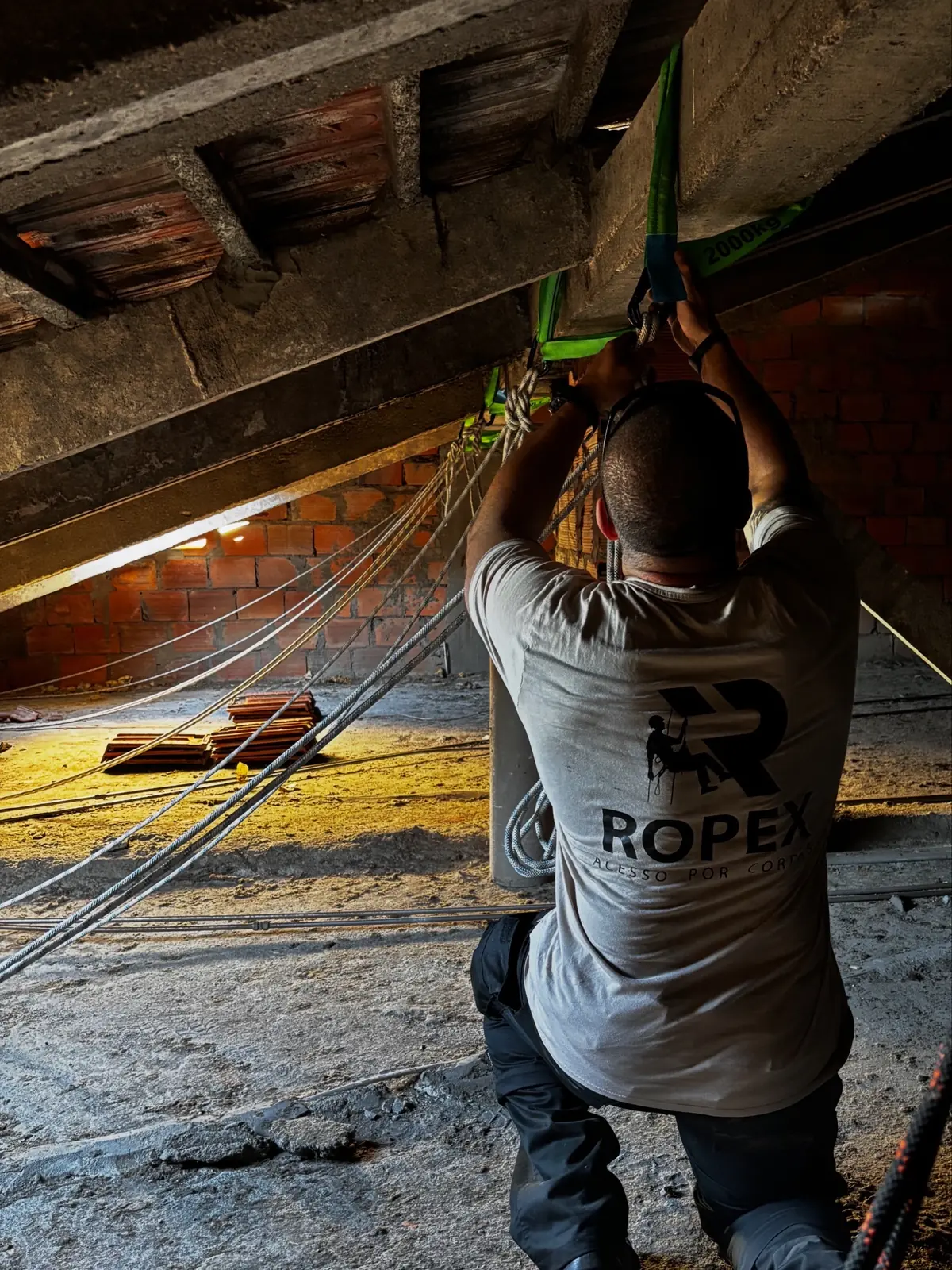 Técnico da RopeX, de costas, a montar a ancoragem das cordas numa viga de betão