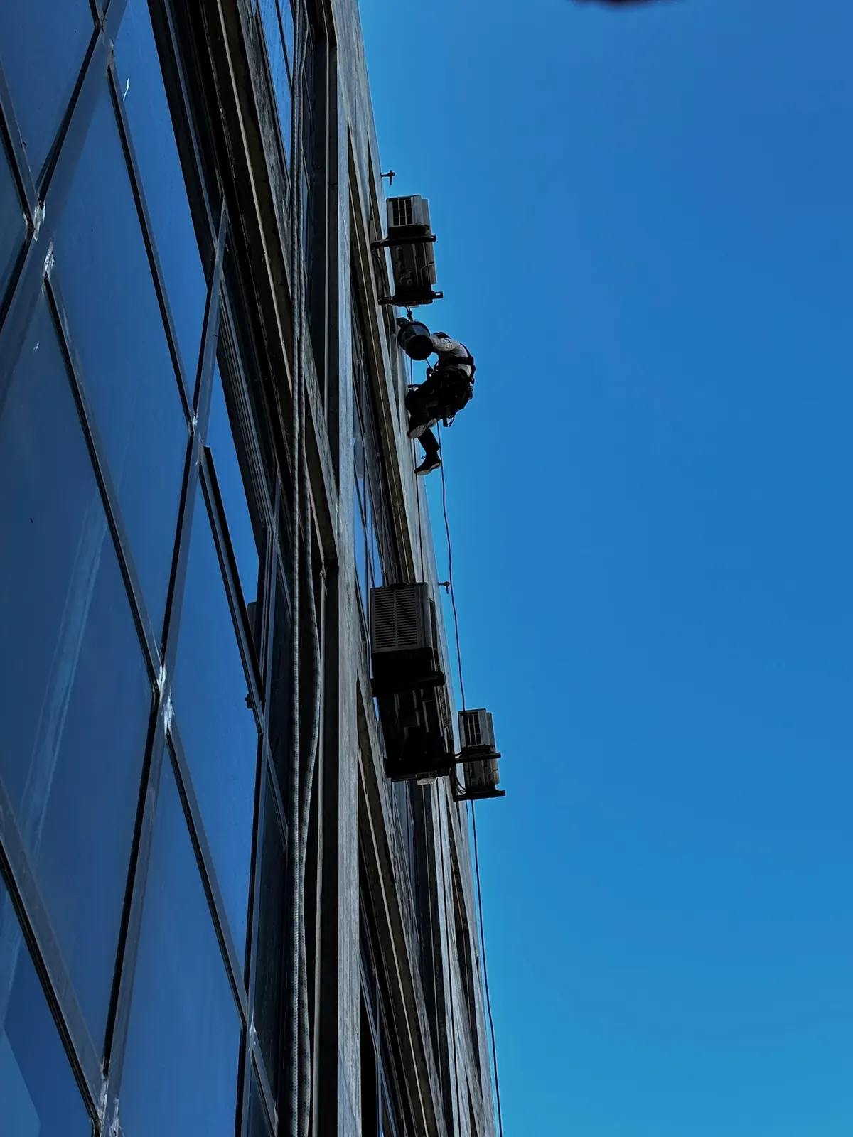 Técnico da RopeX suspenso por cordas junto à fachada envidraçada de um edifício alto