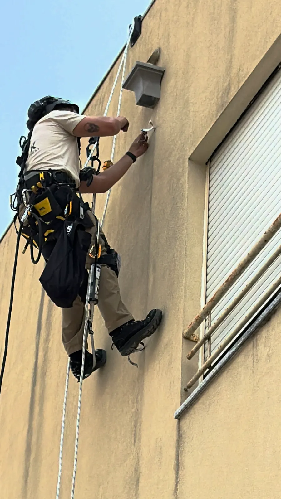 Técnico da RopeX suspenso a trabalhar numa fixação da fachada ao lado de uma janela