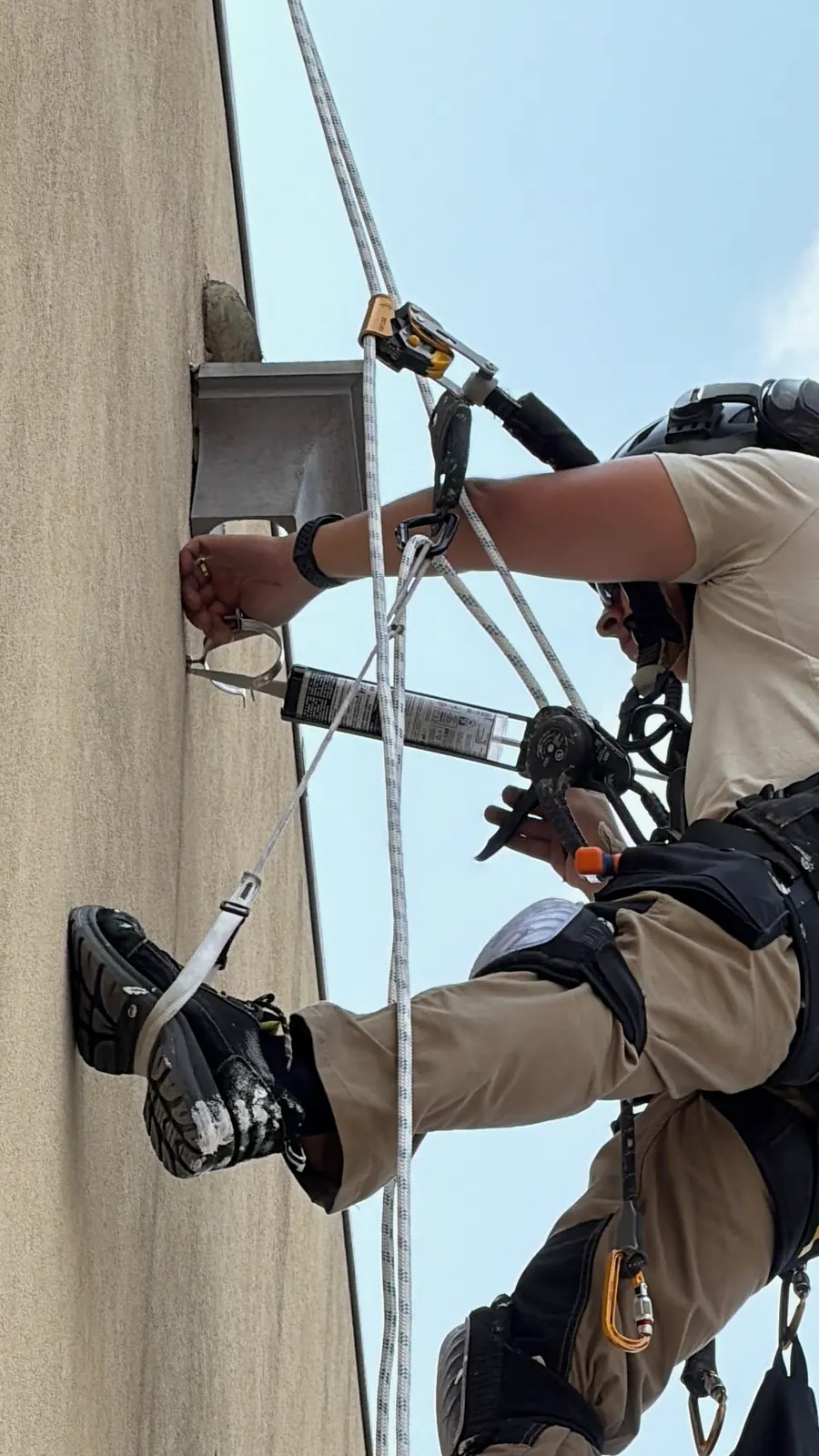 Técnico da RopeX com o pé apoiado na fachada a trabalhar numa fixação metálica