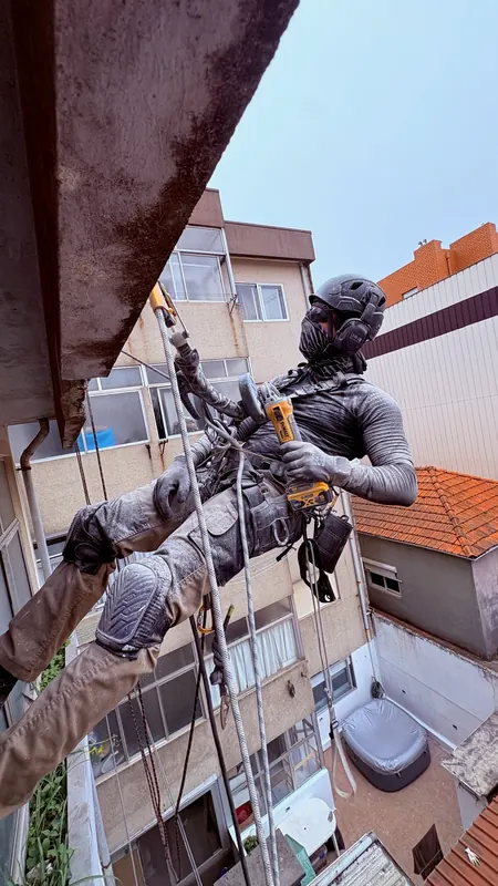 Técnico da RopeX suspenso por baixo da laje de uma varanda a trabalhar o betão com uma rebarbadora