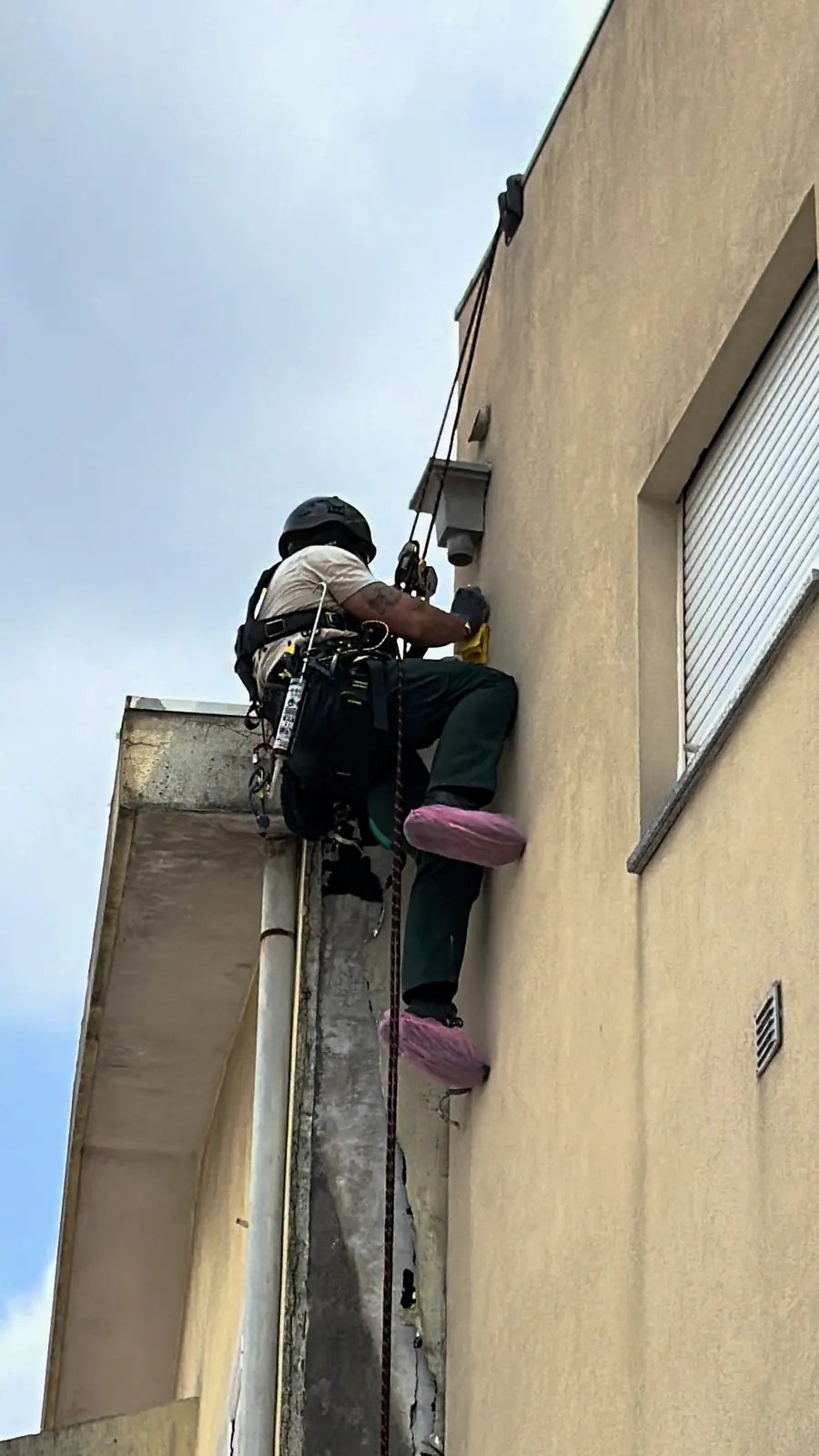 Técnico da RopeX suspenso por cordas junto a uma saída de ventilação, por cima de um tubo de queda e de uma faixa degradada da fachada