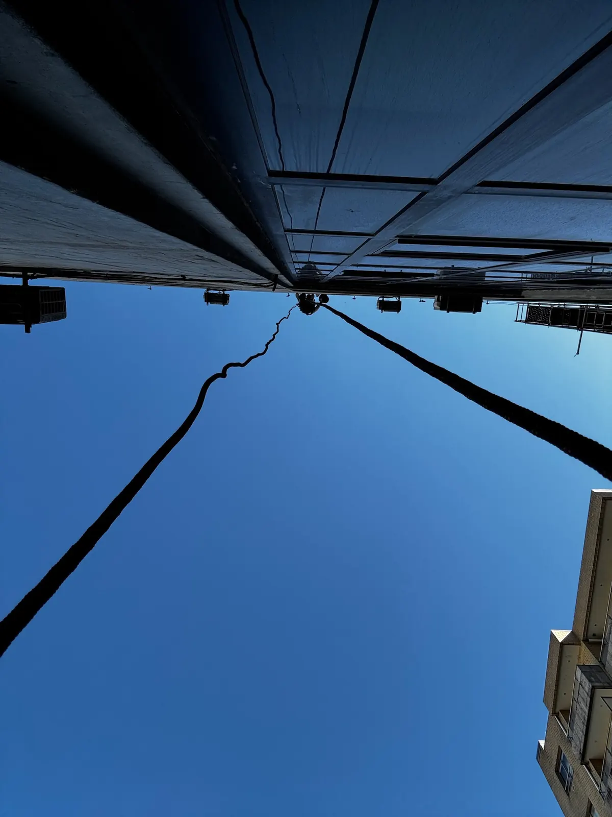 Cordas de acesso vistas de baixo, a subir até ao topo de um edifício contra o céu azul