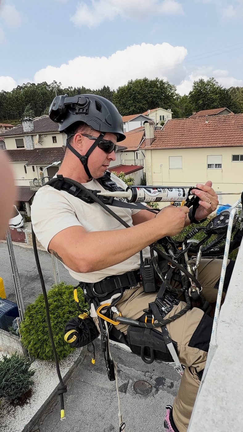 Técnico da RopeX a aplicar vedante numa abraçadeira de tubo de queda, suspenso por cordas