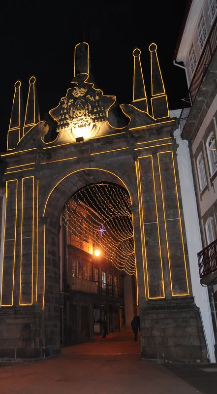Arco da Porta Nova, em Braga, contornado por luzes douradas, com um túnel de luzes na rua por trás