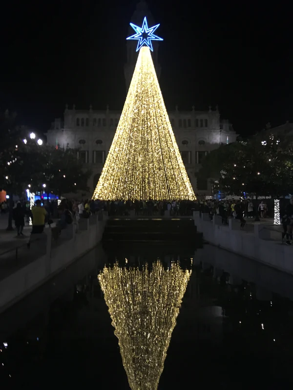 Árvore de Natal de grande porte feita de fios de luz dourada na Avenida dos Aliados, no Porto, refletida no espelho de água