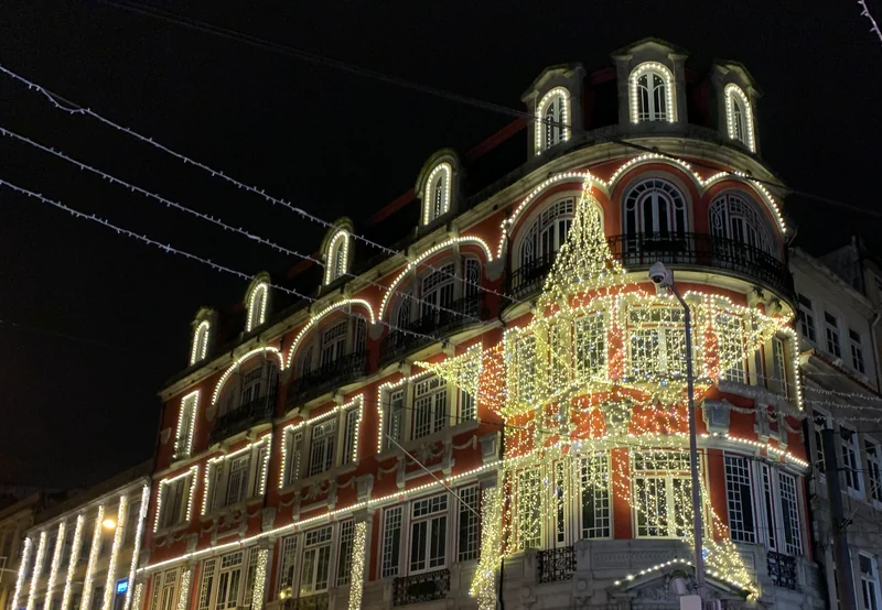Edifício de esquina no Porto com janelas, cornijas e mansardas contornadas por luzes quentes