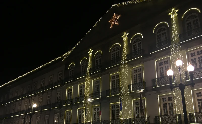 Fachada de um edifício histórico no Porto com cortinas de luz a descer do telhado e estrelas luminosas